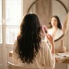 Cascadhe · morning-routine-mirror Cascadhe en routine matinale devant miroir vintage, peignoir soie creme